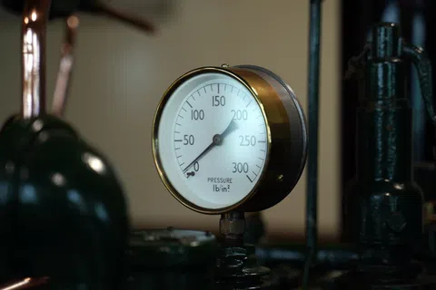 Close-up of a pressure gauge reading around 180 psi attached to industrial machinery with pipes and valves.