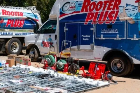 Rooter Plus plumbing trucks with organized plumbing tools and equipment laid out on the ground outdoors.