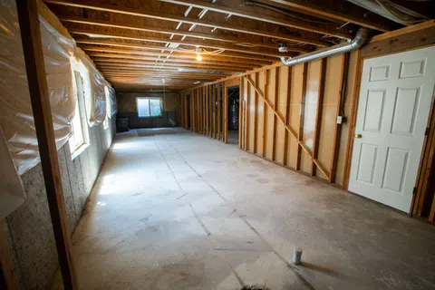 Spacious unfinished basement with bare walls, exposed beams, and concrete flooring, ready for renovation.