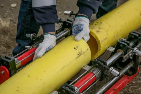 Workers wearing gloves aligning yellow plastic pipes for welding on a machine outdoors