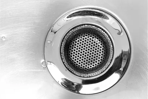 Close-up of a stainless steel sink drain with perforated strainer and circular shiny rim.