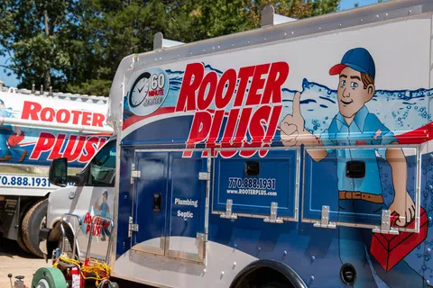 Brightly colored Rooter Plus! plumbing and septic service truck showcasing services in a residential area.