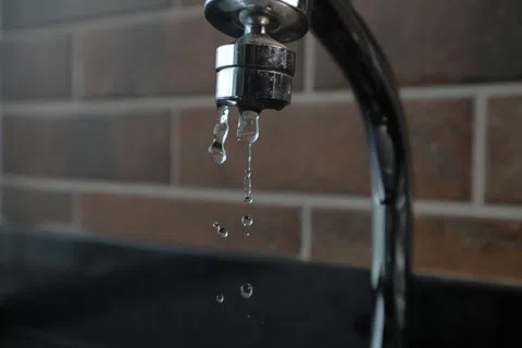 Close-up of a chrome kitchen faucet with water droplets dripping against a tiled backsplash.
