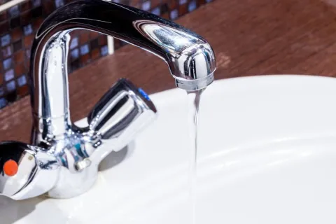 Modern silver faucet with water flowing into a blurred kitchen sink background in soft light.