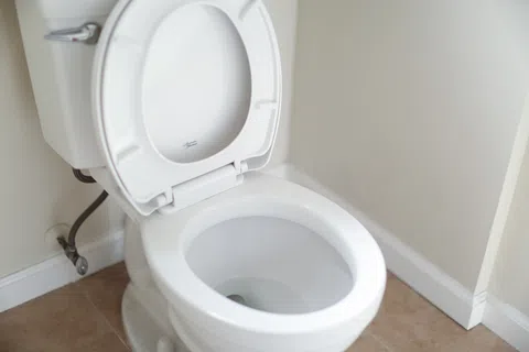 White ceramic toilet with open lid in a clean bathroom with beige tile floor and cream walls.