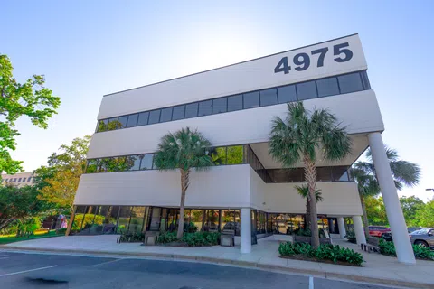 Modern three-story office building with white exterior, palm trees, and large numbers 4975 on top right corner