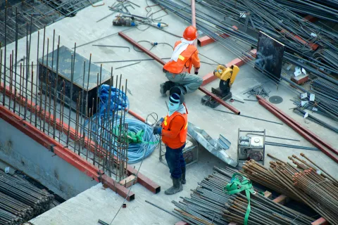 Construction workers in safety gear working on reinforcing steel rods at a building site with concrete floor