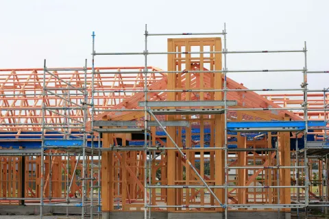 Wooden house framework under construction with scaffolding and clear sky background.