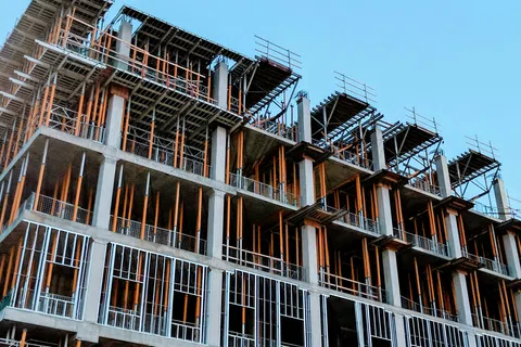 Multi-story concrete building under construction with exposed steel framework and support beams against blue sky.