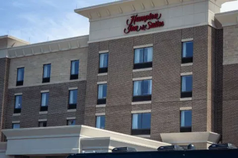 Exterior view of Hampton Inn & Suites hotel building with multiple windows and brick facade under clear sky