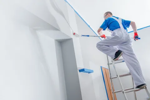 A professional painter in white overalls using a roller on a ladder, illustrating high-quality professional exterior painting for residential homes.