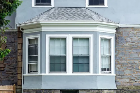 Exterior view of a grey stone and stucco house featuring white historic home windows and a classic bay window design.