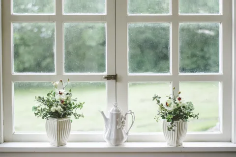a couple of white vases with flowers in them by a window