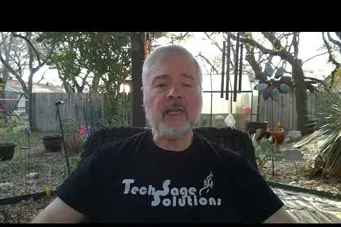Middle-aged man with gray beard wearing a Tech Sage Solutions t-shirt, seated outdoors in a backyard.