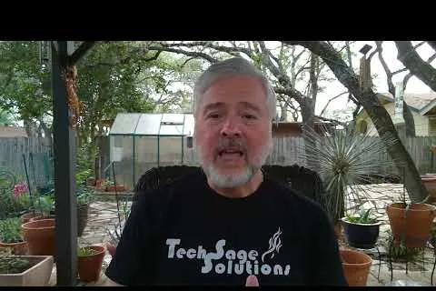Middle-aged man with gray hair and beard wearing a TechSage Solutions shirt speaking outdoors in a garden patio.
