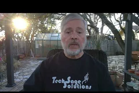 Man with gray beard wearing TechSage Solutions shirt sitting outdoors in a garden during sunset.