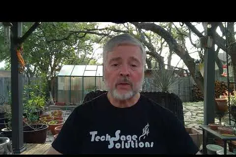 Middle-aged man with gray hair and beard wearing a Tech Sage Solutions shirt sitting outdoors on a patio.