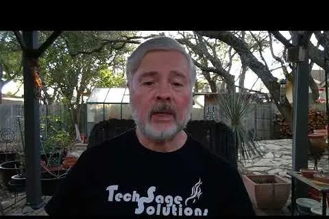 Older man with gray beard speaking outdoors in a garden wearing a Tech Sage Solutions black t-shirt.