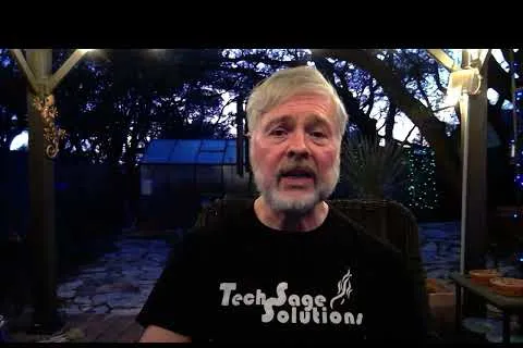 Older man with gray beard speaking outdoors at dusk wearing a Tech Sage Solutions black t-shirt.