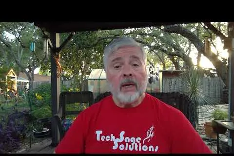 Man with gray hair and beard wearing a red Tech Sage Solutions shirt sitting outdoors in a garden patio.