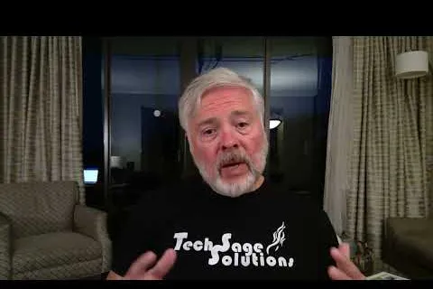 Older man with gray hair and beard speaking indoors wearing a Tech Sage Solutions t-shirt.