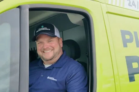 Smiling plumber in blue uniform sitting inside a bright green plumbing service van