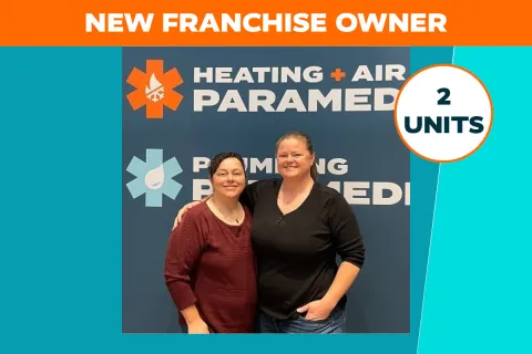 Two smiling women standing together in front of a Heating + Air Paramedics sign announcing new franchise owners in Tucson, AZ.