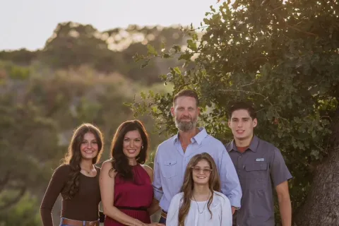 A smiling family poses together outdoors, showcasing a warm, loving atmosphere against natural surroundings.