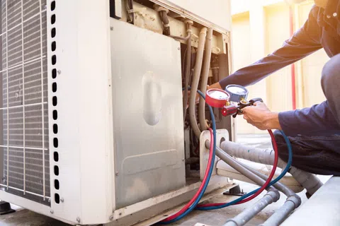 Technician checking and measuring air conditioning system pressure with manifold gauges for HVAC maintenance.