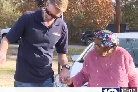 Technician surprising elderly woman with a new HVAC system delivery outdoors near basketball hoop and parked cars