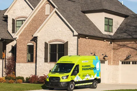 Modern brick and stone house with a bright yellow Plumbing Paramedics van parked in the driveway on a sunny day.