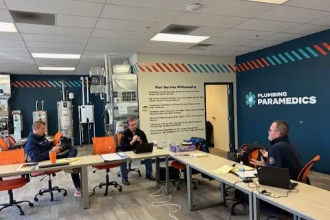 Employees of Plumbing Paramedics collaborate in a modern office space filled with equipment.