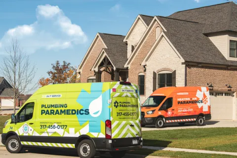 Two service vans parked outside a modern brick house, featuring plumbing and HVAC logos.