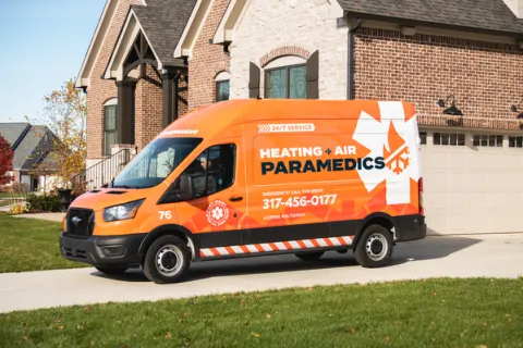Bright orange service van for Heating & Air Paramedics parked in front of a residential home.