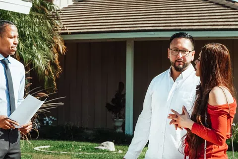 Real estate agent showing a house to a couple having a conversation outside in the yard on a sunny day.