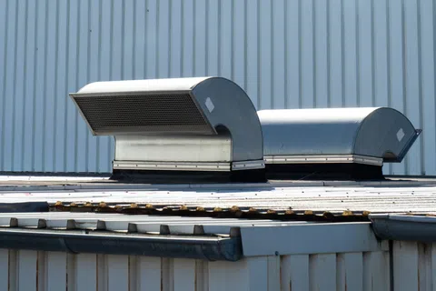 Industrial metal air vents on a corrugated metal rooftop against a striped metal wall background.