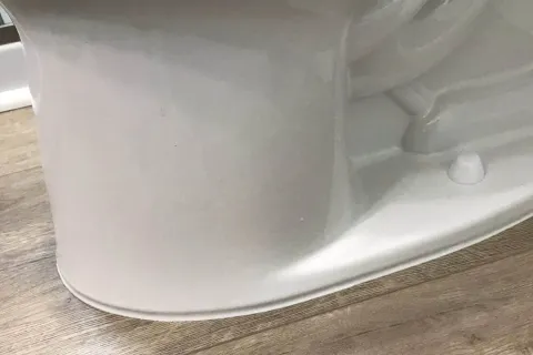Close-up of white toilet base installed on wood-patterned vinyl flooring in bathroom corner.