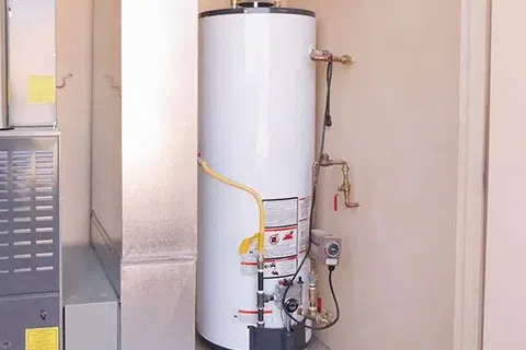 White residential water heater installed next to furnace with pipes and control valves connected