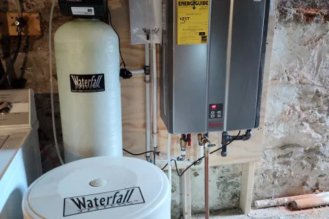 Water heater installation in basement with tank, water softener, and plumbing elements visible.