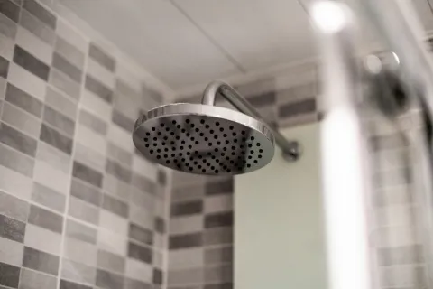 Close-up of a modern round metal showerhead with gray and white tiled wall background in bathroom.