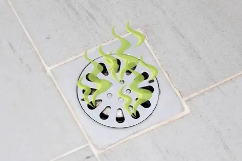Metal drain cover on tiled floor with green odor lines indicating a bad smell or blockage issue.