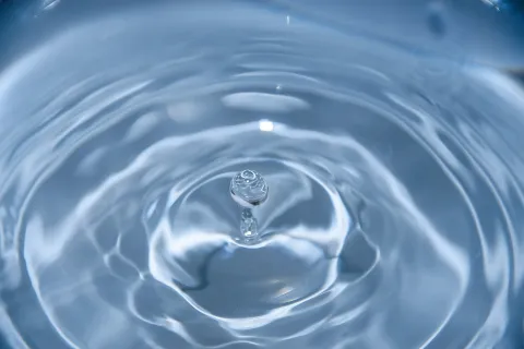 A close-up view of a water droplet creating ripples in a calm blue surface.