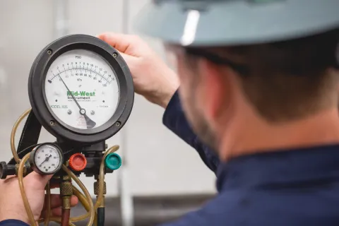 Technician in helmet adjusts pressure gauges on industrial equipment with gas hoses and valves