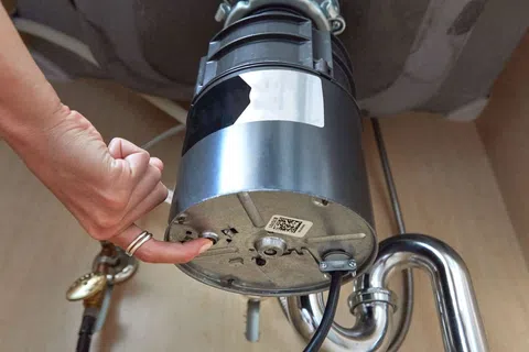 Person using finger to operate a switch on the underside of a kitchen sink garbage disposal unit.