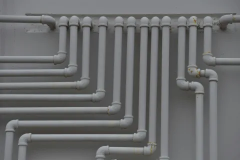 Network of white plumbing pipes with multiple joints mounted on a gray wall in a building.