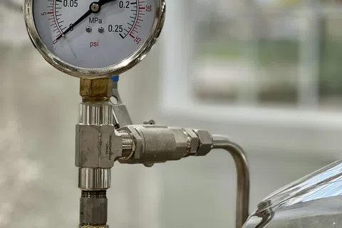 Close-up of a pressure gauge showing readings in MPa and psi attached to metallic pipes and valves.