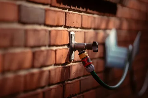 Close-up of an outdoor metal water tap attached to a red brick wall with a green garden hose connected.