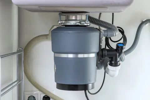 Under-sink garbage disposal unit installed with connected pipes and power supply in kitchen cabinetry.