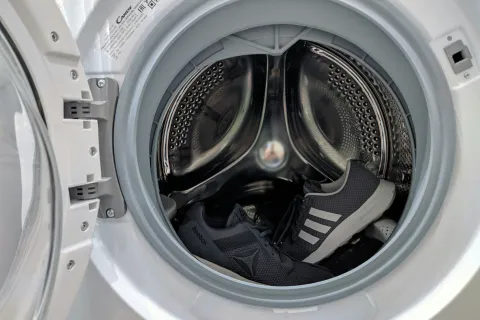 Black Reebok and Adidas sneakers inside the drum of an open front-loading washing machine