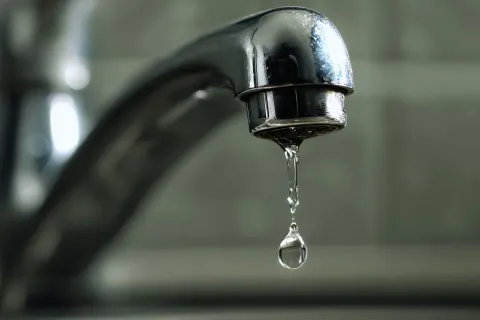 Close-up of a chrome faucet dripping a single water drop against blurred background.